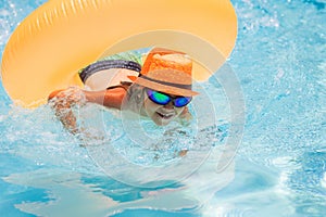 Child in swimming pool on inflatable ring. Kid swim with orange float. Kids beach fun.