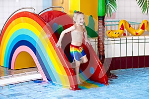 Child on swimming pool slide. Kids swim. Water fun