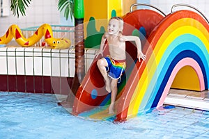 Child on swimming pool slide. Kids swim. Water fun