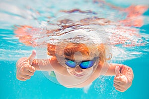 Child in swimming pool underwater with thumbs up. Underwater kid swim in pool. Child boy swimming and diving underwater