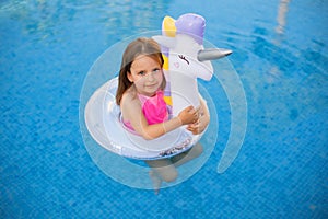 Child in swimming pool on unicorn inflatable violet ring.