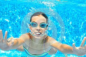 Child swims in pool underwater, funny happy girl in goggles has fun under water and makes bubbles, kid sport