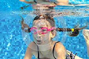 Child swims in pool underwater, happy active girl in goggles has fun in water