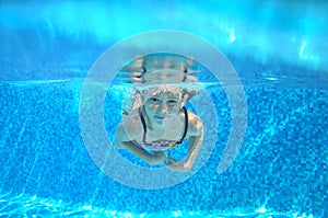 Child swims in pool underwater, happy active girl has fun