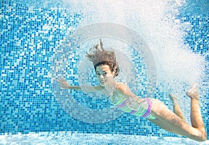 Child swims in pool underwater, happy active girl jumps, dives and has fun under water, kids fitness and sport on family vacation