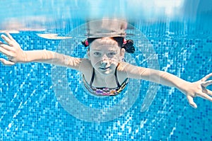 Child swims underwater in swimming pool, active little girl dives and has fun under water, kid fitness and sport