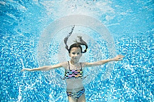 Child swims underwater in swimming pool, active little girl jumps, dives and has fun under water, kid fitness and sport