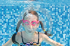Child swims underwater in swimming pool, happy active girl in goggles dives and has fun under water, kid fitness and sport