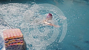 A child in a swimsuit and a bathing cap swimming independently in the pool.