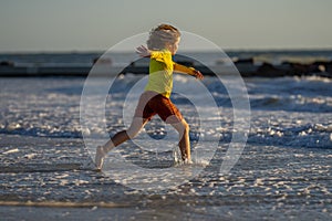 Child in swimwear running into sea water during summer holidays. Child running along ocean. Child on summer beach. Kid