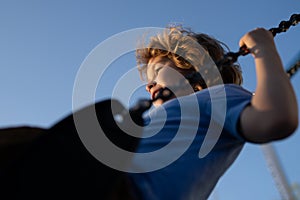 Child swinging on chain swing on city kids playground. Swing ride. Cute child having fun on a swing on summer sky