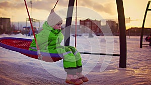 Child swings on round swing on snow-covered Playground in winter.