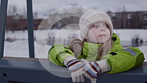 Child swings on a swing in a snow-covered park.