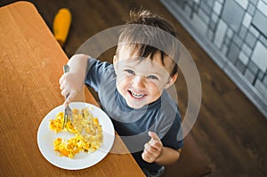A child in a t-shirt in the kitchen eating an omelet, a fork
