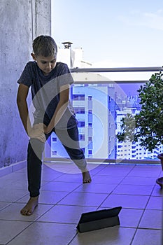 Child with tablet computer doing sport exercises on balcony. Sport, healhty lifestyle, active leisure at home