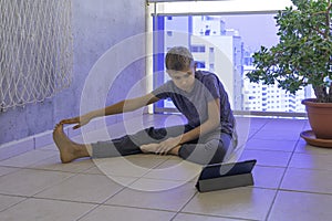 Child with tablet computer doing sport exercises, practicing yoga on balcony. Sport, healhty lifestyle, active leisure