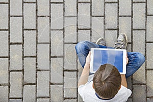 Child with tablet computer sitting outdoors. Education, learning, technology, friends, school concept. Top view.