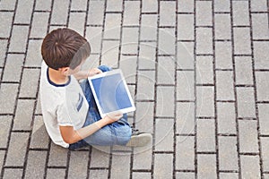Child with tablet computer sitting outdoors. Education, learning, technology, friends, school concept. Top view.