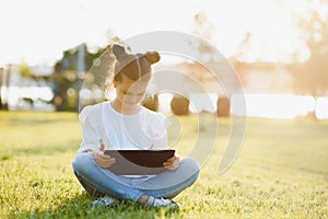 Child with tablet pc outdoors. Little girl on grass with computer