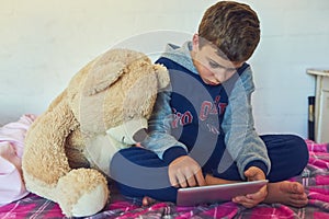 Child, tablet and relax in home bedroom on holiday with education games, app and growth. Online, reading and kid watch a