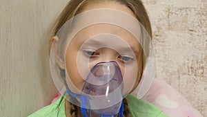 Child with tablet is sick and breathes through an inhaler. Close-up. Little girl treated with an inhalation mask on her