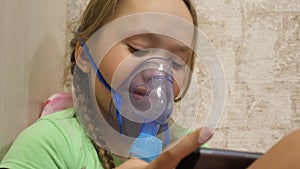 Child with tablet is sick and breathes through an inhaler. close-up. little girl treated with an inhalation mask on her