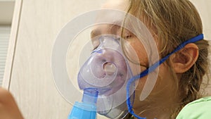 Child with tablet is sick and breathes through an inhaler. Close-up. Little girl treated with an inhalation mask on her