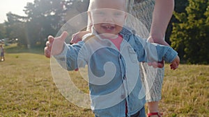 Child takes the first steps walking in the park with mom.