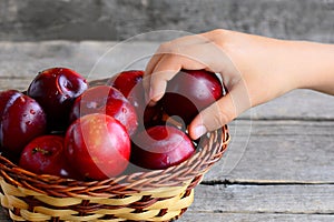 Child takes a plum out of a basket. Fresh juicy plums in a wicker basket on an old wooden table. Healthy eating for kids