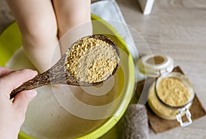 Child taking a healing warming foot bath with mustard powder, adding mustard powder to foot bath with wooden spoon.