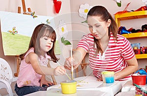 Child with teacher draw paints in play room.