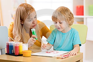 Child with teacher draw paints in play room. Preschool.