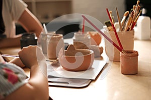 A child with a teacher at a pottery master class. the teacher teaches the child to paint on ceramics.