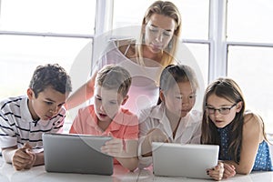 Child with technology tablet and laptop computer in classroom teacher on the background