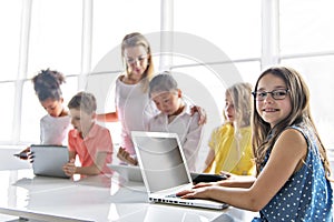 Child with technology tablet and laptop computer in classroom teacher on the background