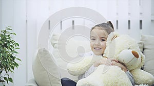 Child and teddy on the sofa. Gorgeous girl is playing with her soft friend.