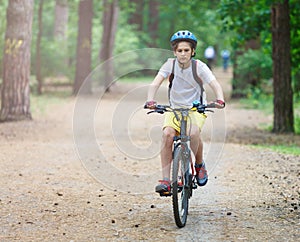 Child teenager on bicycle ride in forest at spring or summer. Happy smiling Boy cycling outdoors in blue helmet. Active lifestyle