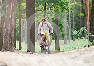 Child teenager in white t shirt and yellow shorts on bicycle ride in forest at spring or summer. Happy smiling Boy cycling