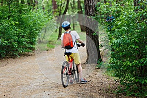 Child teenager in white t shirt and yellow shorts on bicycle ride in forest at spring or summer. Happy smiling Boy cycling