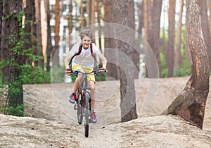 Child teenager in white t shirt and yellow shorts on bicycle ride in forest at spring or summer. Happy smiling Boy cycling outdoor