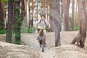 Child teenager in white t shirt and yellow shorts on bicycle ride in forest at spring or summer. Happy smiling Boy cycling outdoor