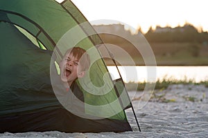 Child in tent yawns. Early morning at the campsite. Camping