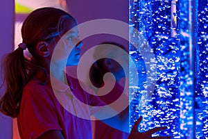 Child in therapy sensory stimulating room, snoezelen. Child interacting with colored lights bubble tube lamp during therapy. photo