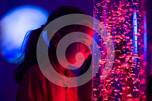 Child in therapy sensory stimulating room, snoezelen. Child interacting with colored lights bubble tube lamp during therapy. photo