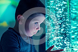 Child in therapy sensory stimulating room, snoezelen. Child interacting with colored lights bubble tube lamp during therapy. photo