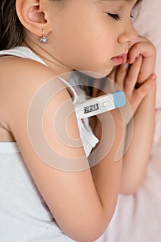 A child with a thermometer lies sick in his bed. The baby has a high body temperature.