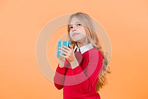 Child with thinking face hold blue cup on orange background