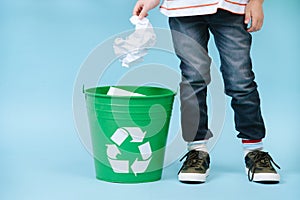 Child is throwing crumpled paper in recycling bin.