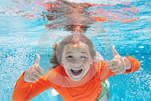 Child with thumbs up swim and dive underwater in the swimming pool.