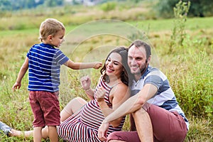 Child tickles his pregnant mother a blade of grass